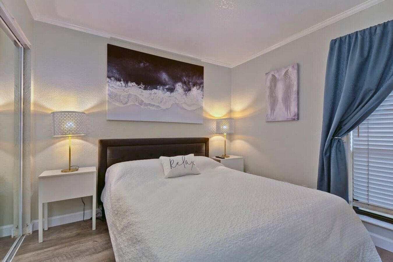 Een slaapkamer met een groot bed, twee nachtkastjes met lampen, een bijzettafeltje, een schilderij aan de muur en een raam met gordijnen.