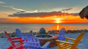 A sunset view with a fire pit and colorful Adirondack chairs on a sandy beach. - Direct water view from Balcony-Pool (Tampa)