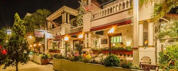 A hotel with a classical facade, outdoor seating, and well-lit surroundings.