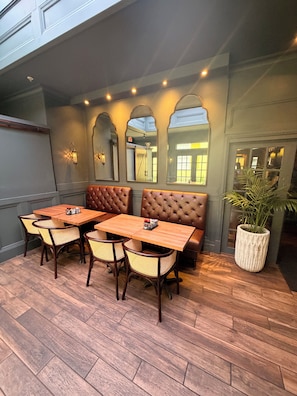 A restaurant with wooden tables and cushioned booths, a potted plant, and a large mirror on the wall. - Casablanca Inn on the Bay (St. Augustine)
