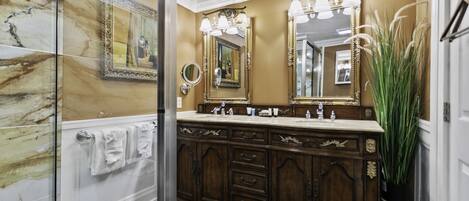 Une salle de bain avec un mur en marbre, un grand miroir, un meuble-lavabo et une plante en pot.