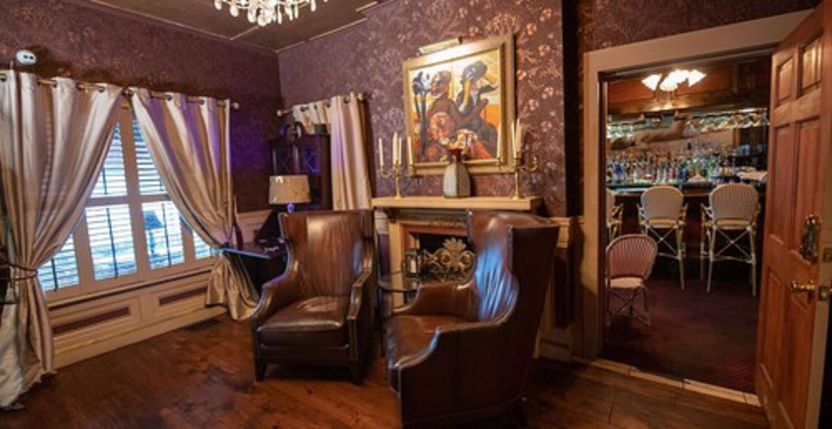 A room with a fireplace, leather chairs, a bar area, and a painting on the wall.