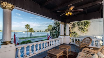 A covered balcony with wicker furniture, a view of the sea, and a flag.