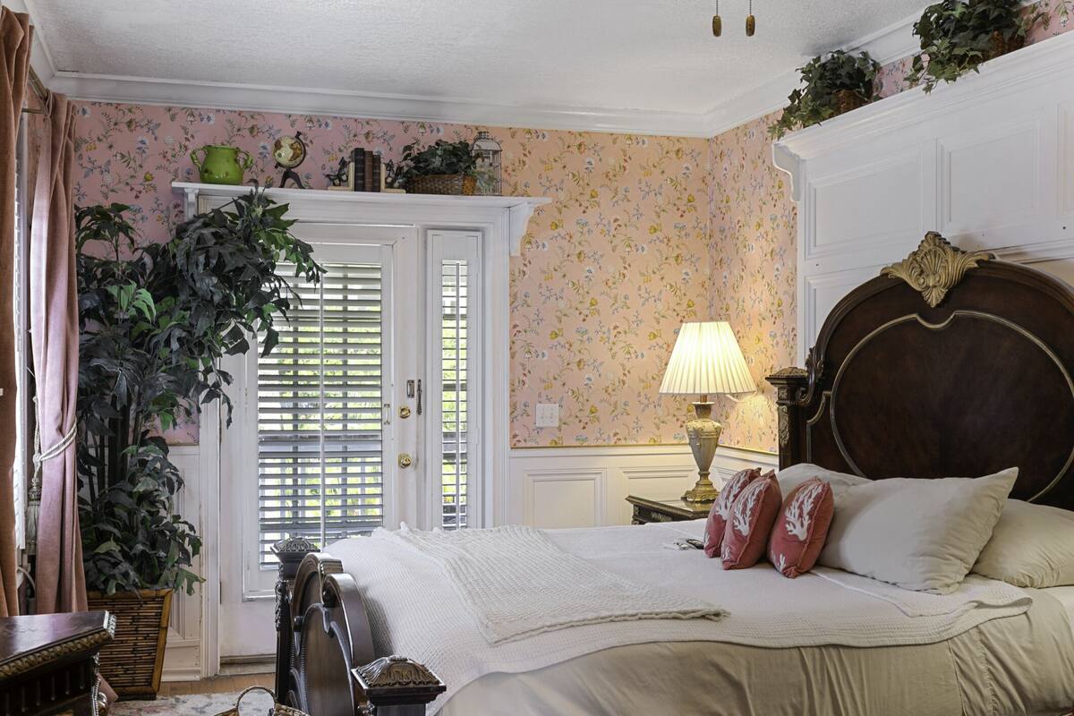 Un dormitorio con cama, cómoda, lámpara y una planta grande en maceta.