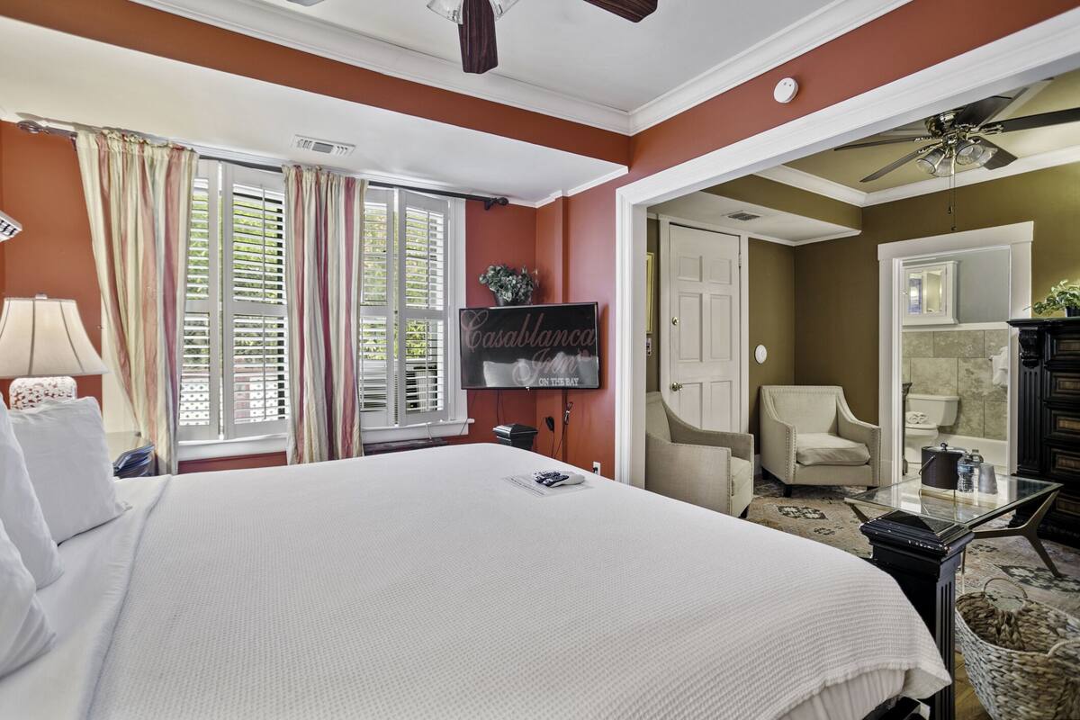 Habitación de hotel con una cama grande, un televisor montado en la pared, una silla y un escritorio con lámpara.