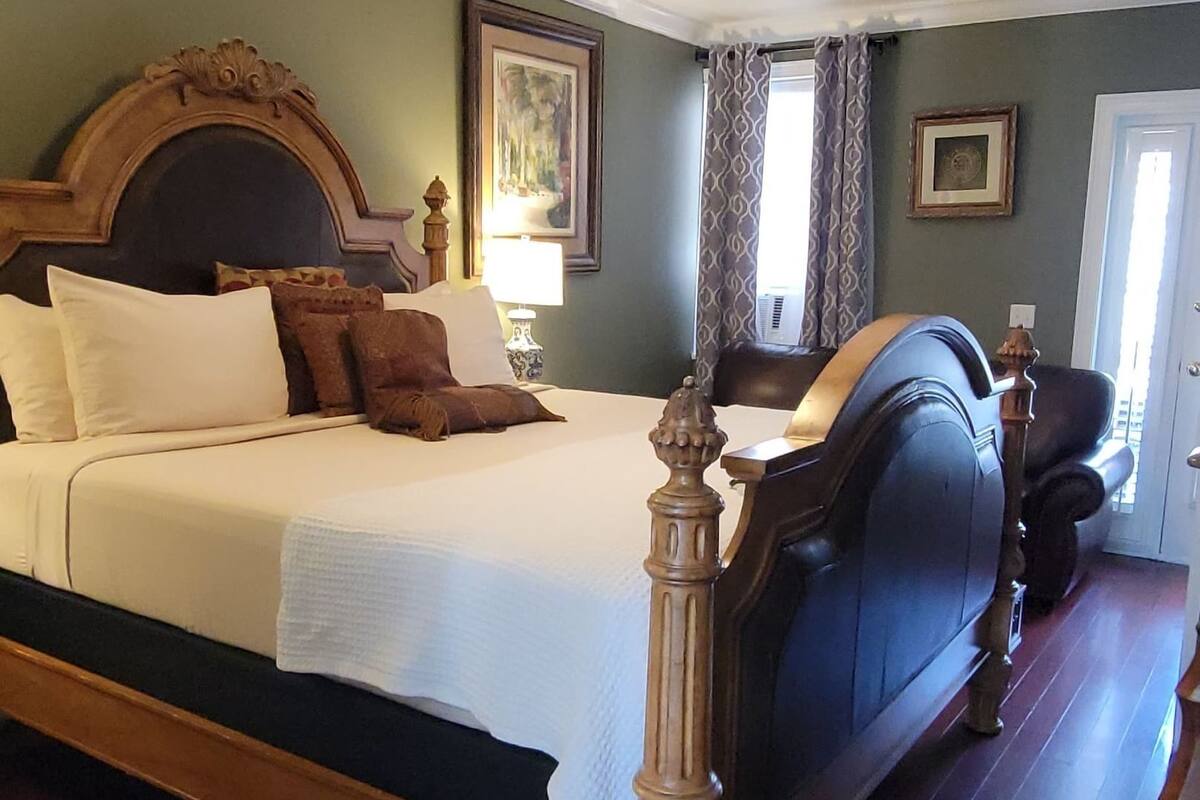 Una cama grande con cabecera de madera, una mesita de noche, una lámpara y un cuadro enmarcado en la pared.