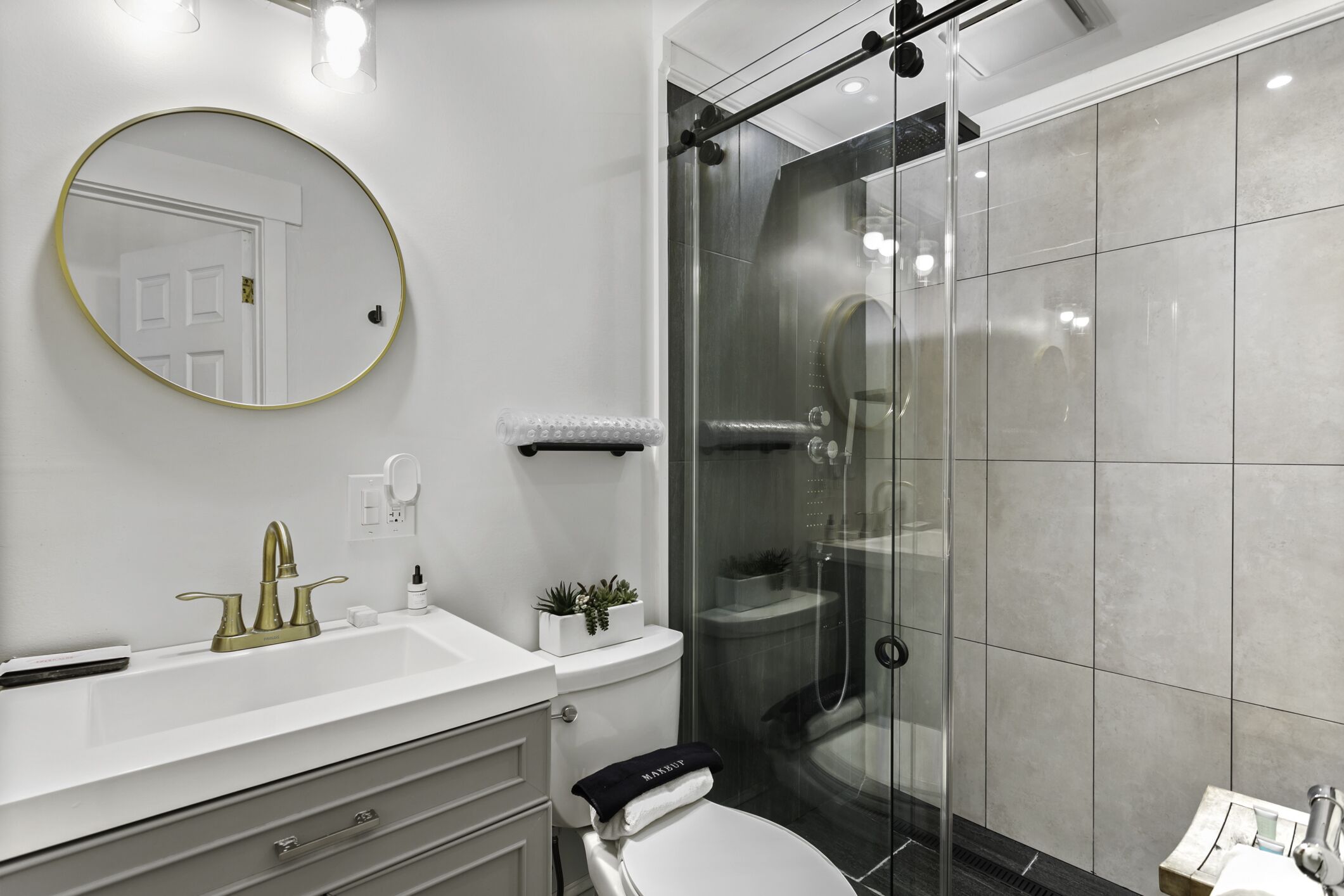 Un baño moderno con lavamanos blanco, grifo dorado y cabina de ducha con paredes de vidrio.