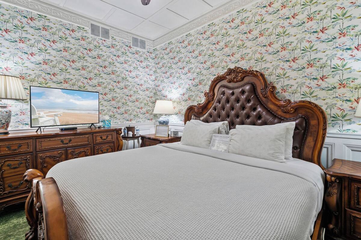 Una habitación de hotel con una cama grande, un televisor sobre una cómoda de madera y papel tapiz floral.