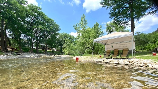 A clear river with rocks, a tent with chairs, and trees in the background.