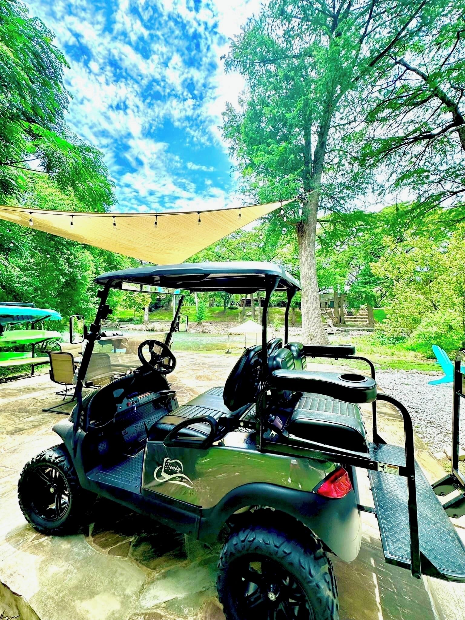 A golf cart parked under a canopy in a park setting.