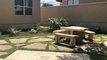 A patio with a stone table and bench, surrounded by a garden with grass and plants.