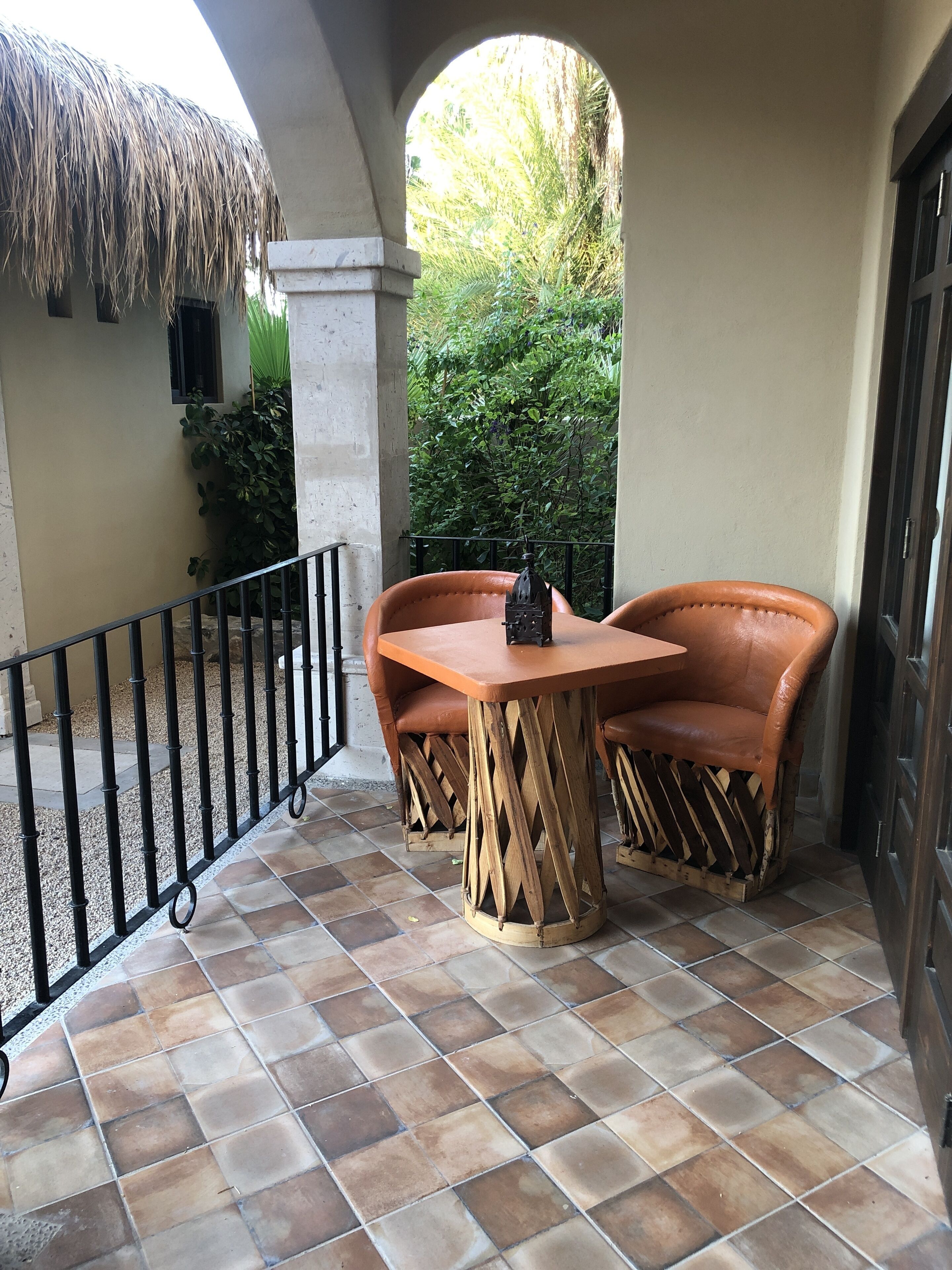 Eine Terrasse mit Fliesenboden, zwei Ledersessel, einem Holztisch und einem Reetdach.