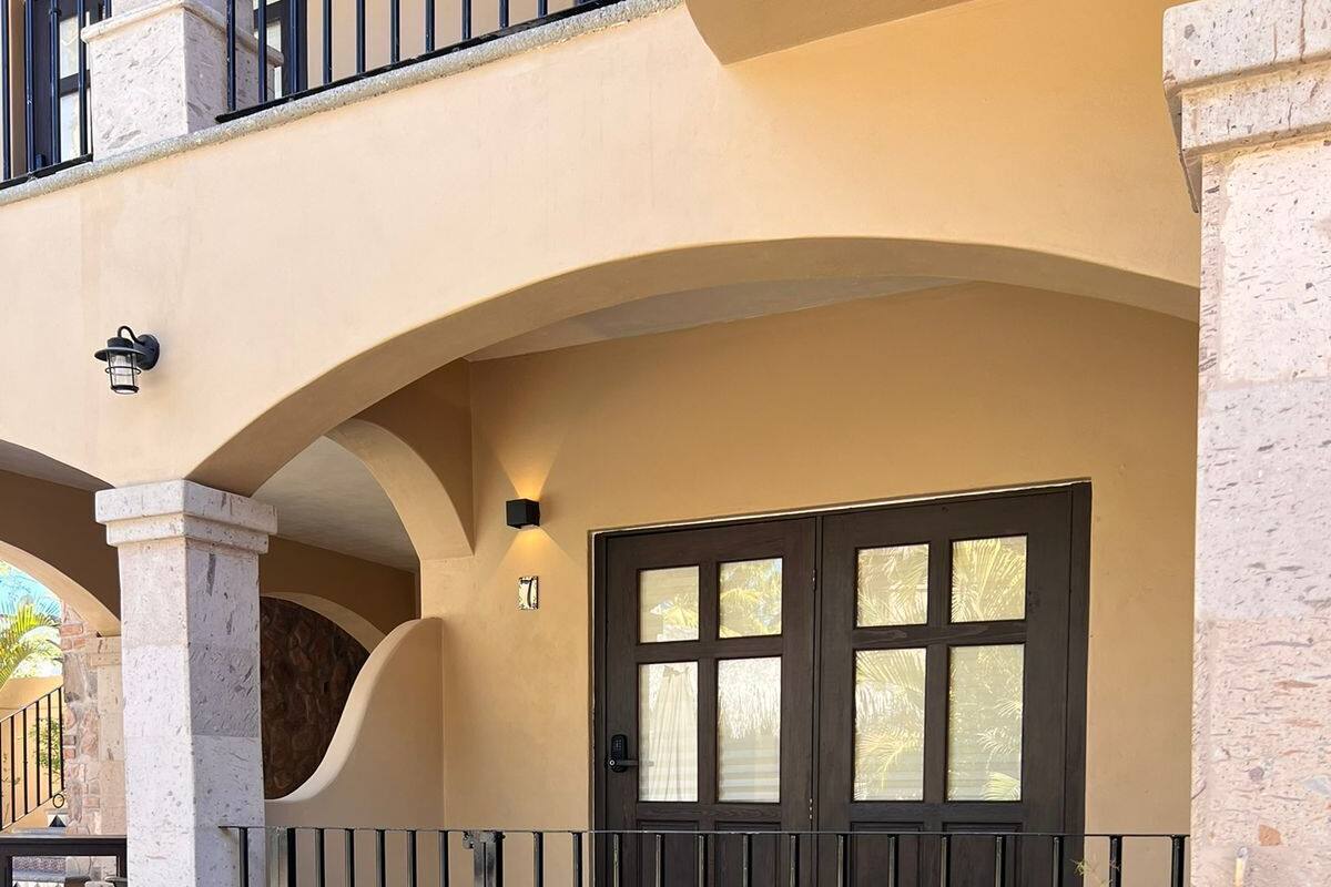 A sunlit outdoor seating area with a lounge chair and a small table, a dark door with glass panels, and a stone balustrade.