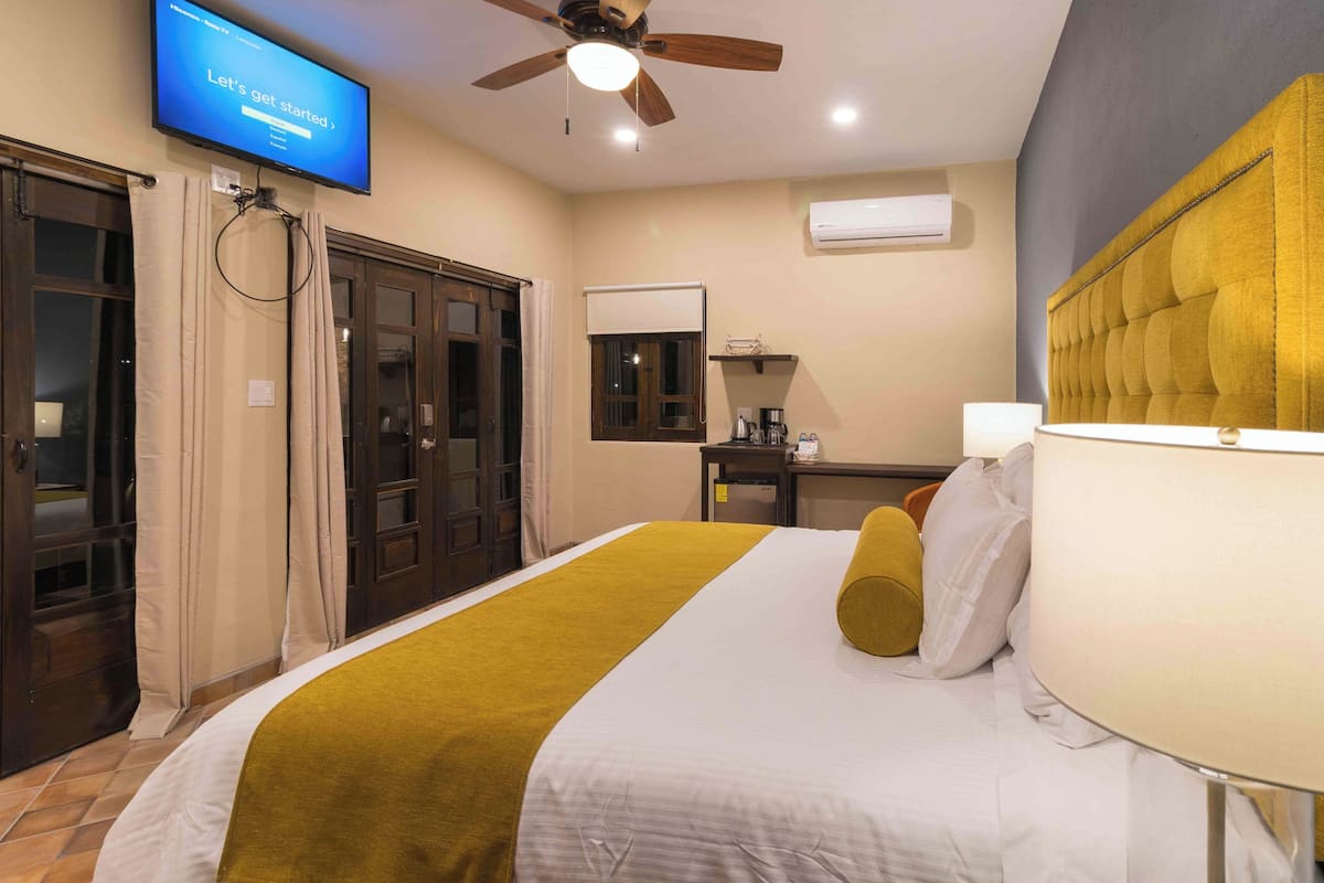 A hotel room with a bed, a television mounted on the wall, a ceiling fan, and an air conditioning unit.