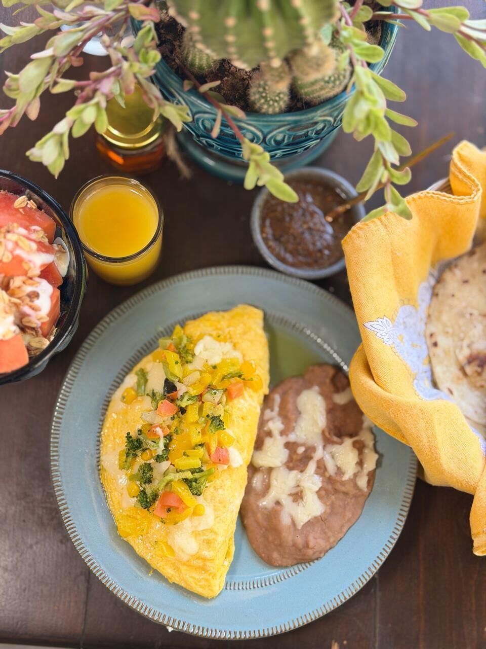 A plate with an omelette, beans, and a side of fruit salad.