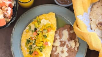A plate with an omelette, beans, and a side of fruit salad.