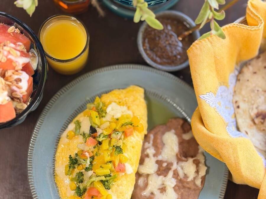 A plate with an omelette, beans, and a side of fruit salad.
