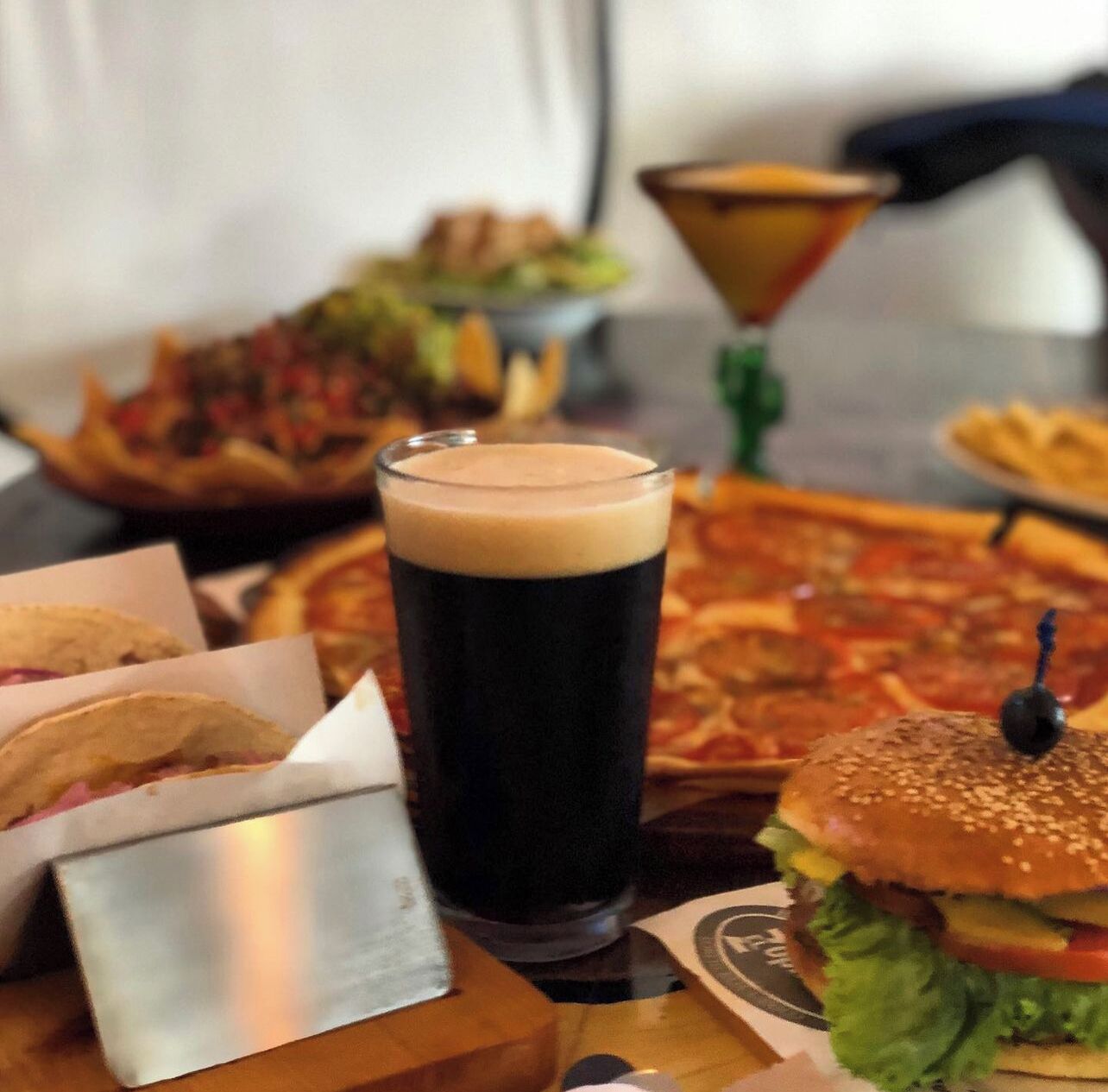 A meal with a burger, a glass of dark beer, and a pizza.