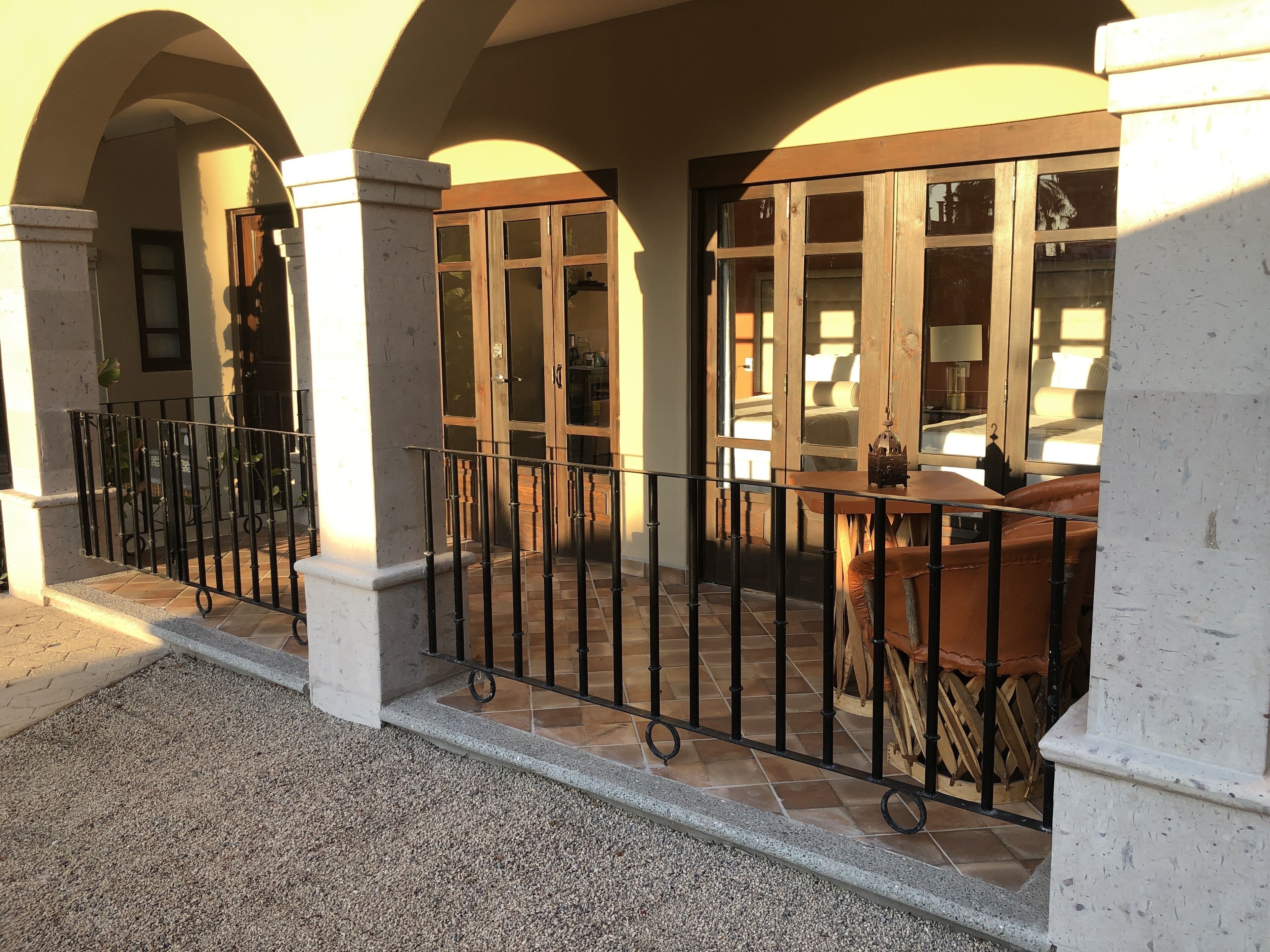 Un espacio al aire libre cubierto con suelo de baldosas, baranda de metal y una mesa de madera con sillas.
