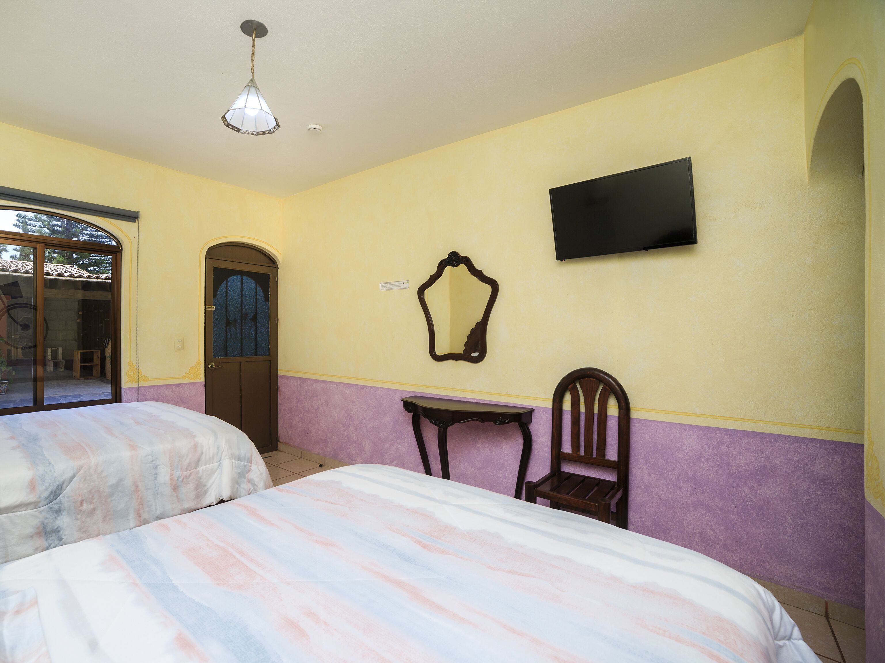 A room with two beds, a television mounted on the wall, a small table, and a chair.