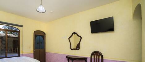 A room with two beds, a television mounted on the wall, a small table, and a chair.