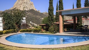 Piscina com montanha ao fundo, rodeada por vegetação e um edifício com telhado vermelho.