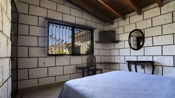 Un dormitorio con una cama, una silla, un televisor y una ventana.