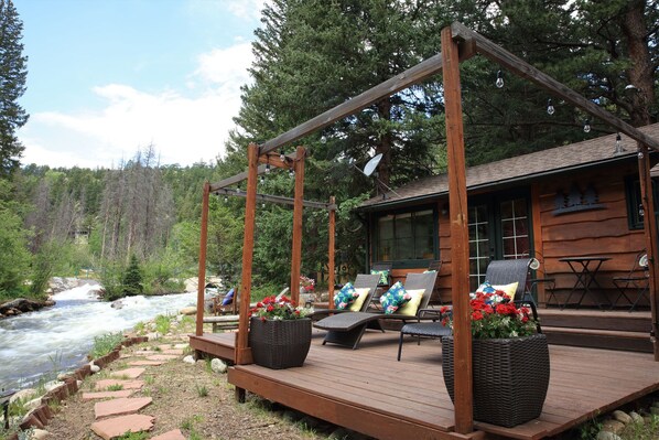 A wooden deck with outdoor seating, a river view, and a cabin with a satellite dish.