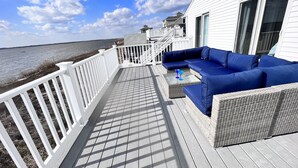Una terraza con barandilla blanca, un sofá azul y una mesa de vidrio con dos vasos azules.
