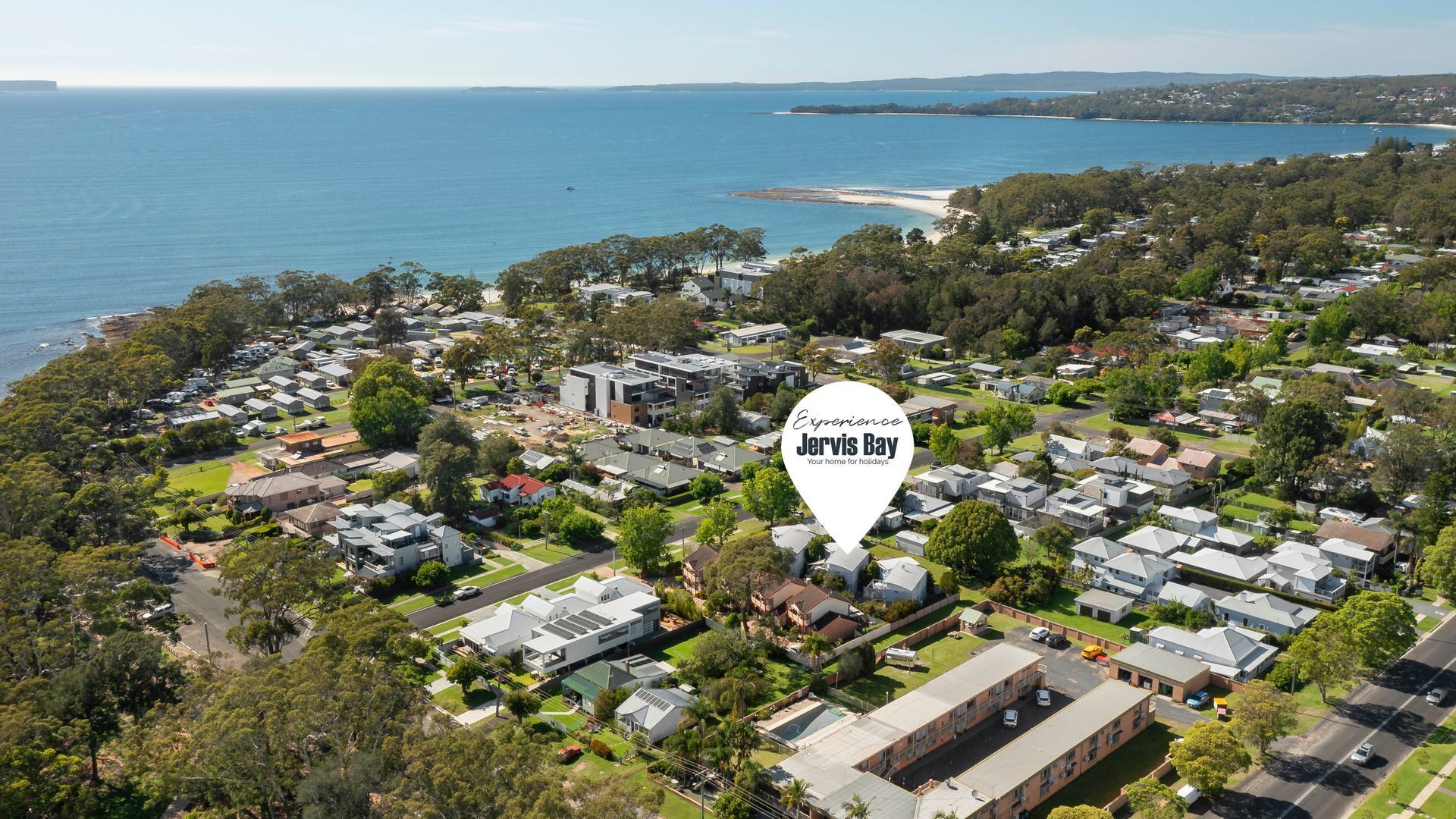 An aerial view of a residential area with houses, roads, and a beach in the background.