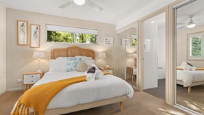 A bedroom with a bed, bedside tables, a window, and a mirror. - White Sands Deck House by Experience Jervis Bay (Huskisson)