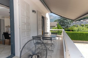 A balcony with a table and chairs, a door, and a view of a residential area with houses and greenery.
