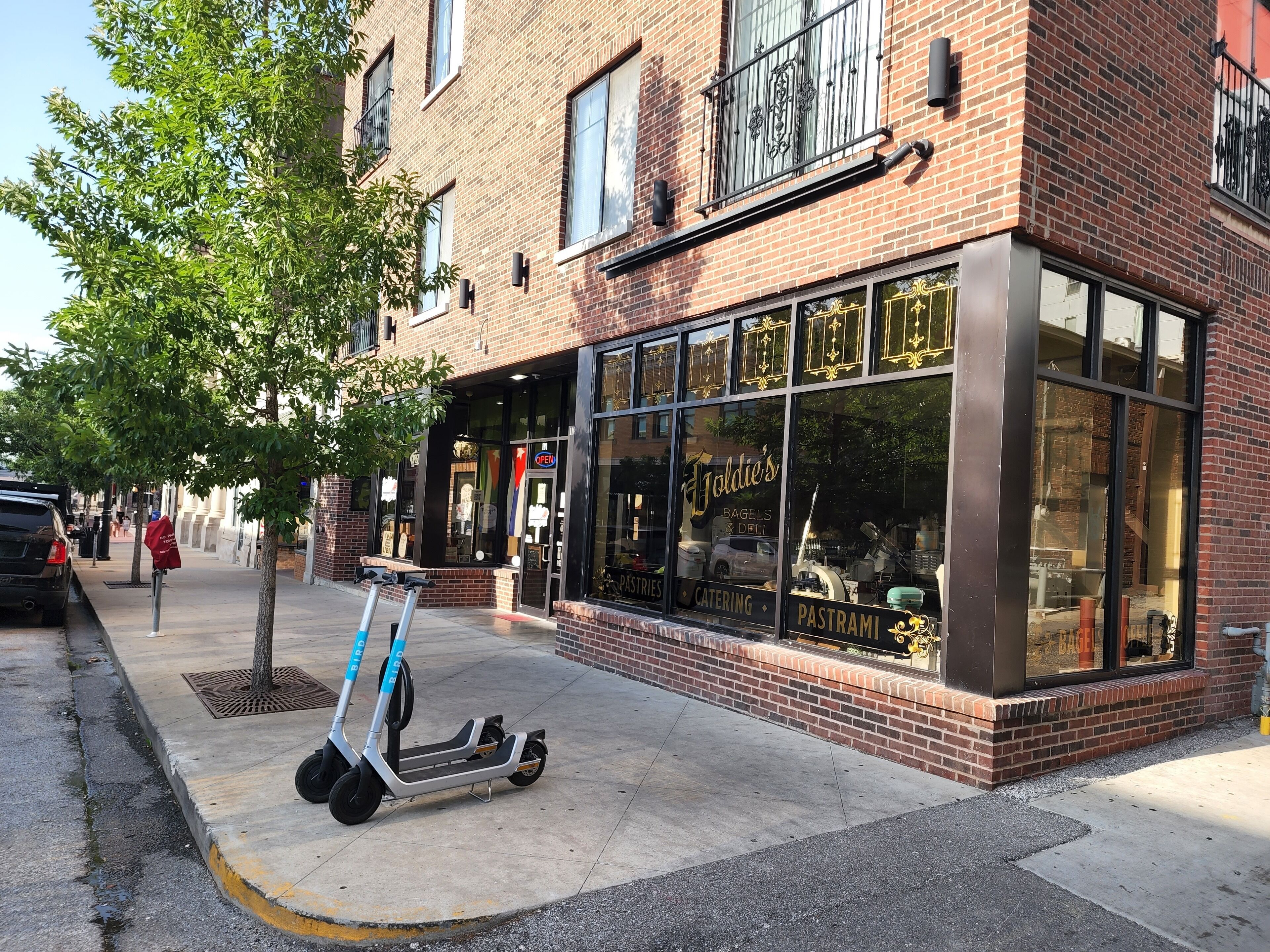 Een winkelgevel met grote ramen, een bordje met 'Joldie's Bagels & Deli' en een geparkeerde elektrische scooter.