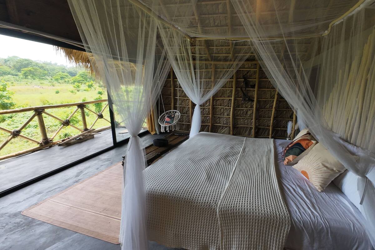 A bed with a mosquito net, a wooden floor, and a view of the outdoors.