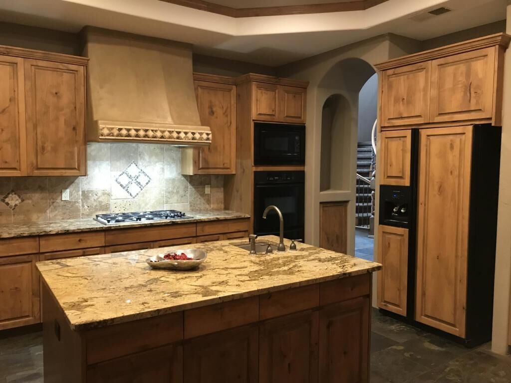 A kitchen with wooden cabinets, a granite countertop, a built-in microwave, and a stainless steel sink.