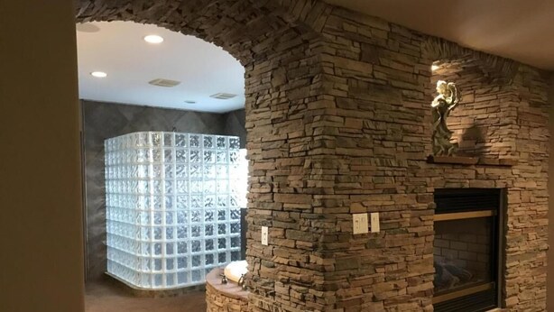 Une cheminée en pierre agrémentée d’une sculpture décorative, un mur en blocs de verre et un luminaire encastré au plafond.