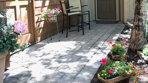 A residential entrance with a wooden door, a small porch with two chairs, and a number sign above the door. - Tiny Condo, Quietly Nestled in Sun Valley                                        (Sun Valley)