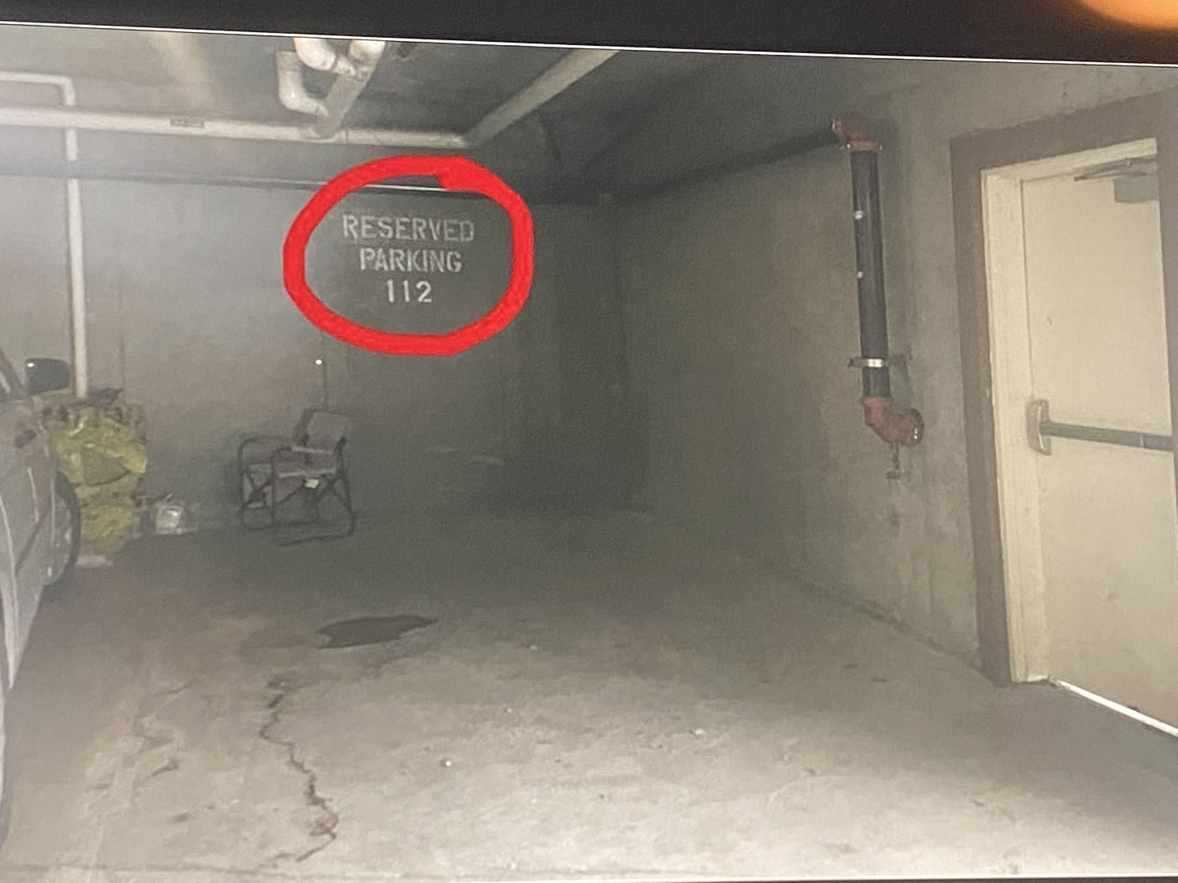 Un parking peu éclairé, avec un panneau indiquant que la place numéro 112 est réservée.