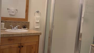 Een badkamer met een houten wastafelmeubel, een wastafel, een spiegel met verlichting, een handdoekhouder en een douche met glazen wanden.