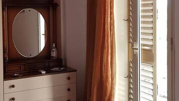 Una camera da letto con un letto, una cassettiera con specchio, una finestra con tende e una porta con persiane.