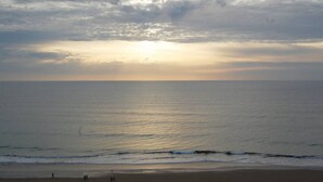 A beach with a sunset over the ocean, calm waves, and a few people walking on the sand. - Apartamento Playa Victoria Cadiz (Cádiz)
