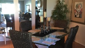 A dining area with a glass-top table surrounded by wicker chairs, a potted plant, and a framed picture on the wall. - Close To Anna Maria Island, Beaches. On IMG Golf Course. Short Drive To Sarasota (Bradenton)