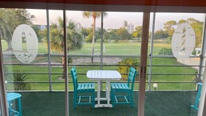 Een balkon met een tafel en stoelen, uitzicht op een golfbaan en een palmboom.