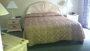 Une chambre à coucher avec une tête de lit en bois, un lit recouvert d’une couvre-lit à motifs, deux tables de chevet avec des lampes, une commode et une fenêtre avec des rideaux.