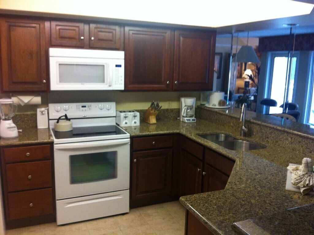 A kitchen with wooden cabinets, a microwave, a stove, a coffee maker, and a sink.