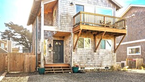 Una casa a due piani in legno con un balcone, un portone e un piccolo portico.