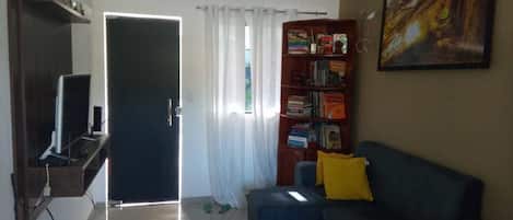 Una sala de estar con sofá, estantería, televisor y puerta que da al exterior.