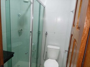 A small bathroom with a glass shower enclosure, a white toilet, and a wooden door. - Apartamento Aconchegante (Manaus)