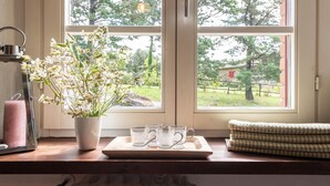 A window with a view of greenery and a building, a potted plant with flowers, a tray with glasses, and a candle. - 3 bedroom awesome home in Sassetta (Sassetta)