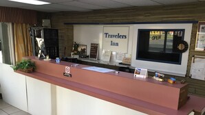 Un comptoir d’accueil à l’hôtel Travelers Inn, avec une pancarte indiquant qu’il n’y a ni remboursement, ni possibilité d’annulation, et que les paiements par carte Visa ou en espèces sont privilégiés.